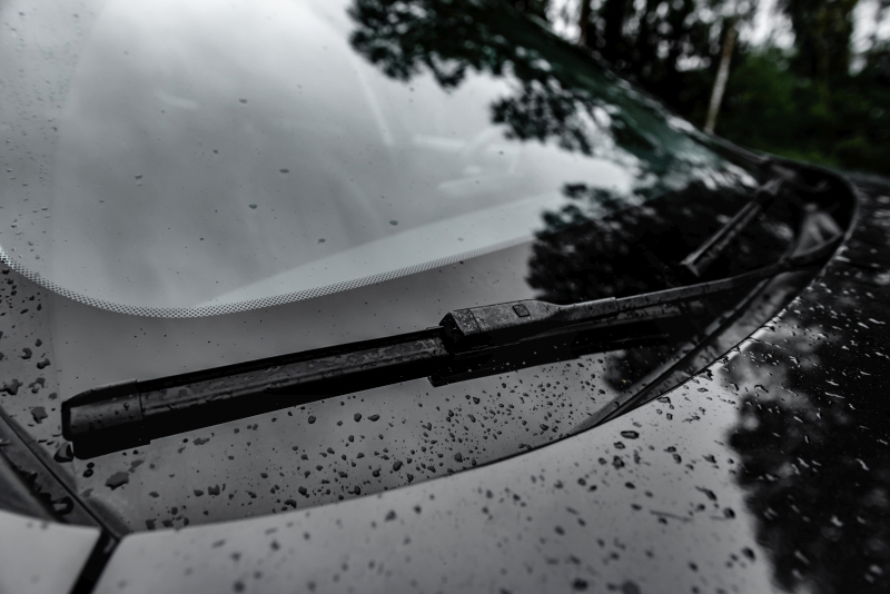 Kvapky dažďa na čelnom skle auta so stieračom počas daždivého počasia.